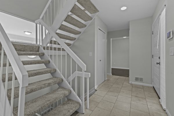 Modern interior with beige tiled floor and carpeted stairs; neutral walls and white door add brightness.