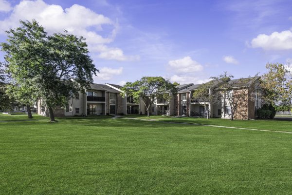 Modern apartment complex surrounded by lush green lawn under a blue sky.