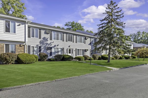 Two-story apartment building with well-kept lawns and trees under a clear blue sky.