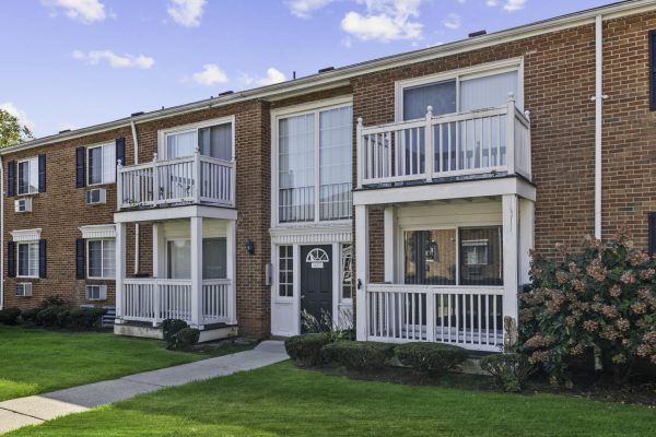 Brick apartment building with balconies, green lawn, and bright blue sky background.