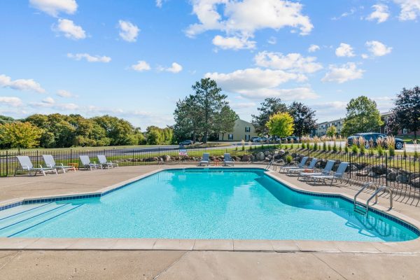 Outdoor swimming pool with lounge chairs and lush greenery under a bright blue sky.