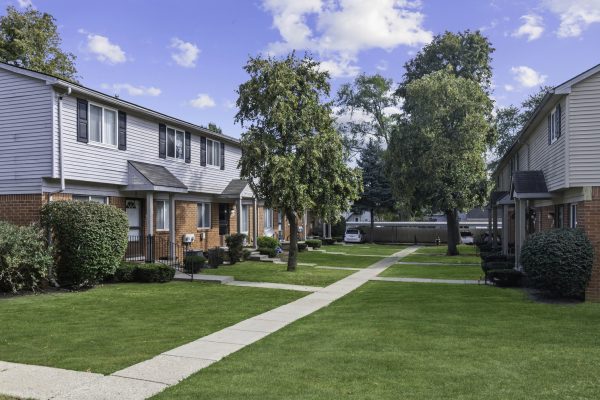 Row of suburban townhouses with well-kept lawns and trees on a sunny day.