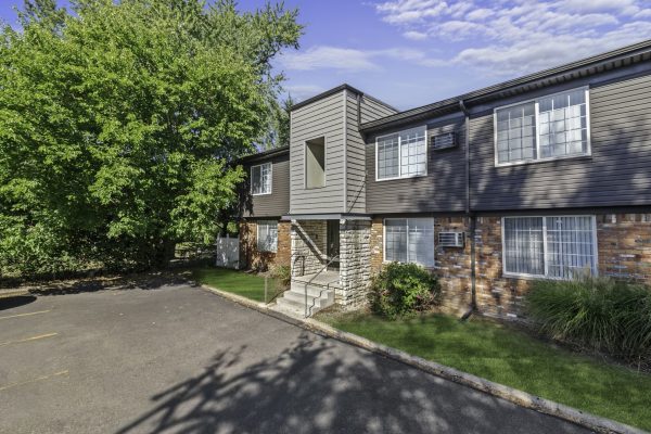 Apartment building exterior with green lawn and trees under a clear blue sky.