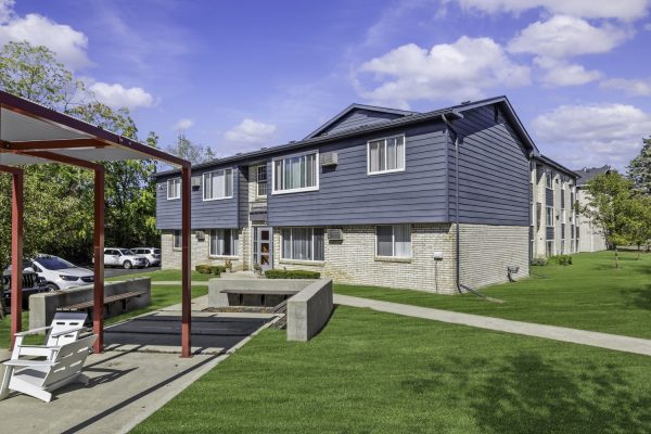 Modern blue and white apartment building with lawn, picnic area, and parking under a clear sky.
