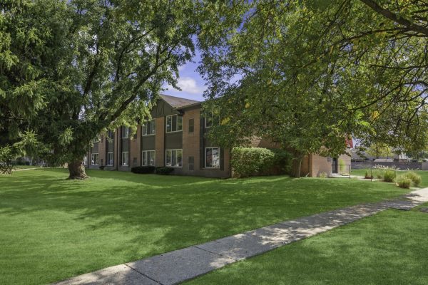 Lush green lawn with trees and a brick building under a clear blue sky.