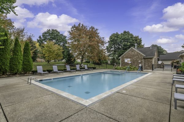 Outdoor swimming pool with lounge chairs, surrounded by trees and blue skies, perfect for relaxation and leisure.
