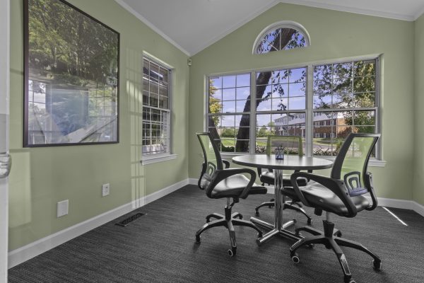 Modern meeting room with large windows, green walls, and round table with chairs, creating a bright, airy workspace.