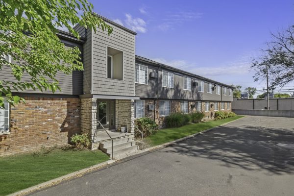 Two-story brick building with modern siding, green lawn, and a clear blue sky in a suburban setting.