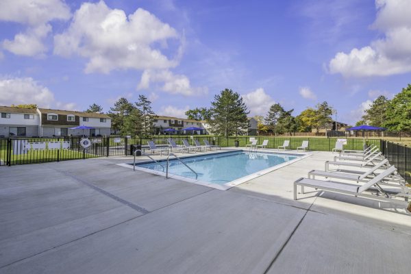 Outdoor pool with lounge chairs and residential buildings in the background on a sunny day.