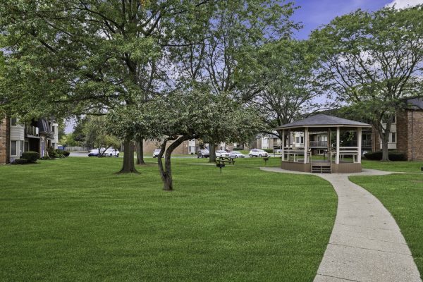 Community park with gazebo, lush green grass, trees, and surrounding residential buildings on a clear day.