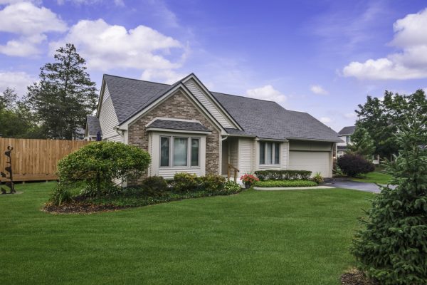 One-story suburban house with brick facade and manicured lawn under a blue sky.