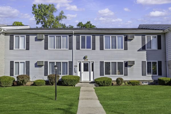 Gray two-story apartment building with green lawn and pathway, under a blue sky.
