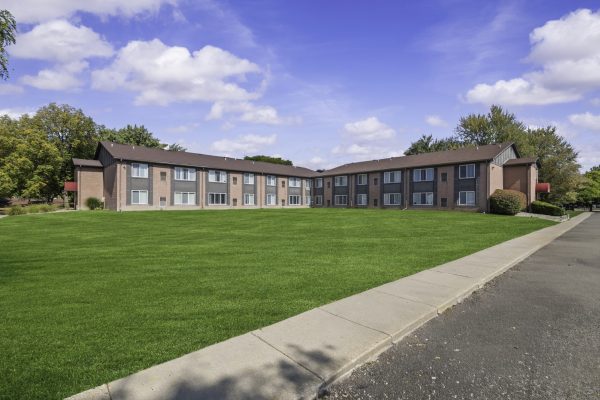 A two-story brick apartment complex with manicured lawn under a blue sky and scattered clouds.