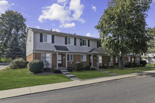 Red brick townhouse with green lawn and large tree on a sunny day.
