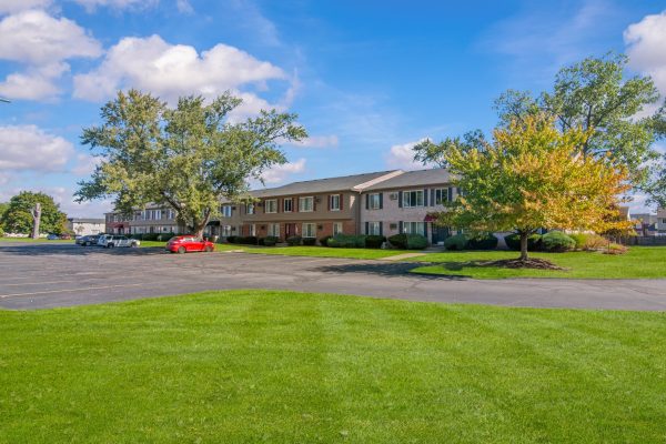 Sunny day view of suburban townhouses with green lawns, parking area, and vibrant trees.