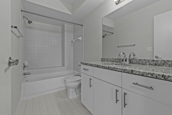 Modern bathroom with white tiles, granite countertop, and shower-tub combo.