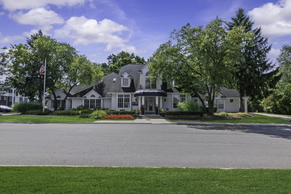 Elegant house with lush landscaping, American flag, blue sky, and vibrant garden in front.