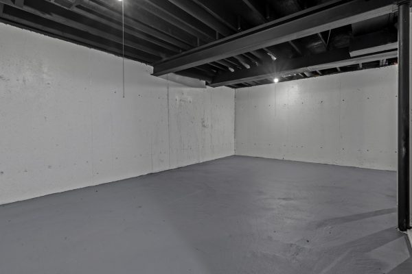 Empty basement with concrete walls and floor, exposed ceiling beams, ideal for renovation or storage space.