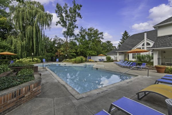 Outdoor pool area with loungers, umbrellas, and surrounding greenery under a clear blue sky.