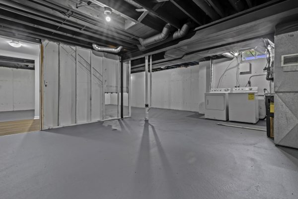 Unfinished basement with washer and dryer, exposed pipes, and concrete floor in a residential home.