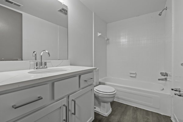 Modern white bathroom with sleek fixtures, wood flooring, and a clean design featuring a sink, toilet, and bathtub.