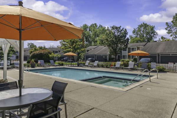 Outdoor pool area with sun loungers and orange umbrellas, surrounded by greenery and residential buildings.