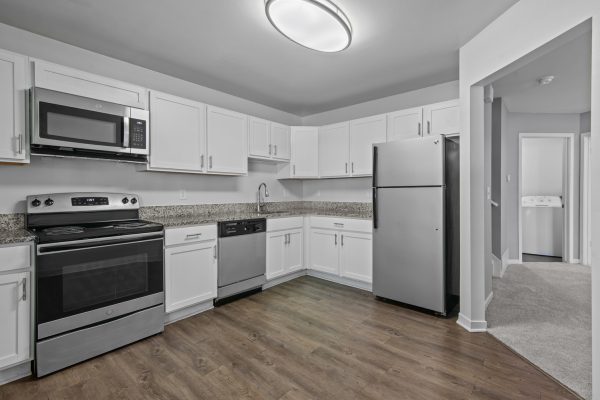Modern kitchen with stainless steel appliances, white cabinets, and wood flooring.
