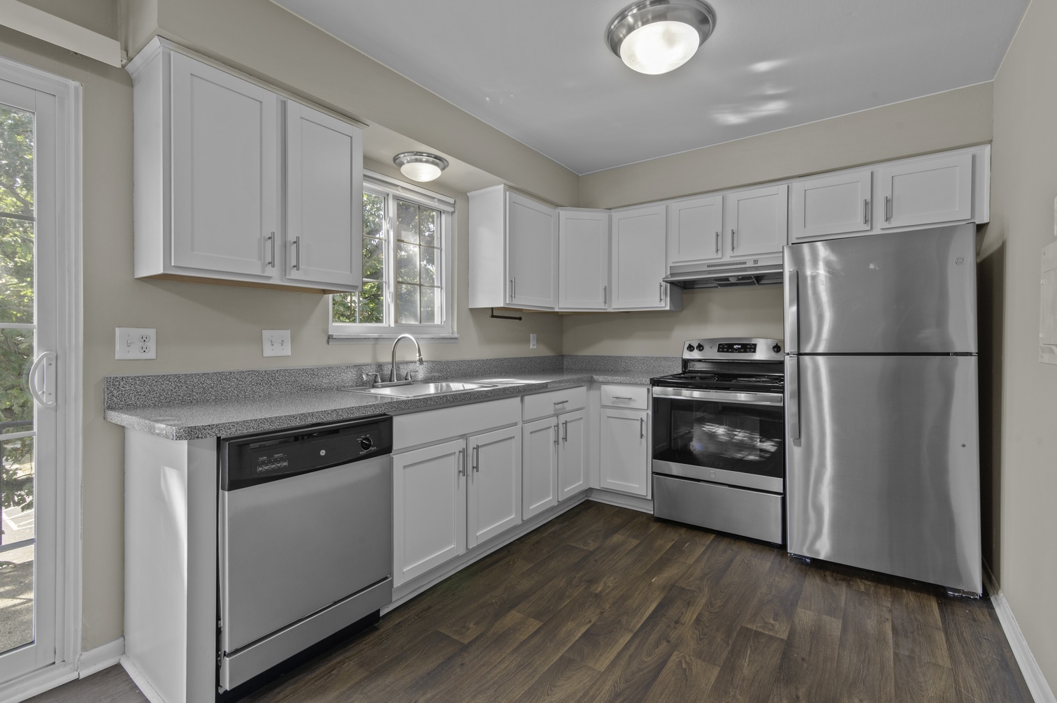 Modern kitchen with white cabinets, stainless steel appliances, and wood flooring. Bright natural light through window.