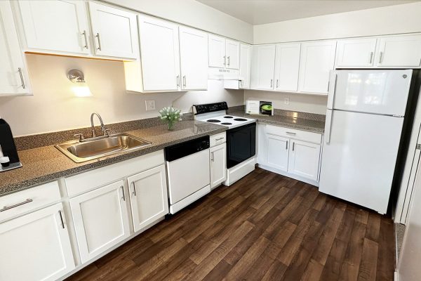 Modern kitchen with white cabinets, granite countertops, wooden floor, coffee maker, and appliances.