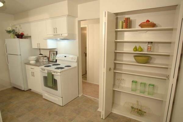 Modern kitchen with white cabinets, stove, and open pantry shelves holding bowls, jars, and decorative items.