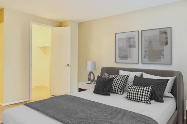 Modern bedroom with grey upholstered bed, patterned pillows, and abstract wall art. Bright open door to a closet.