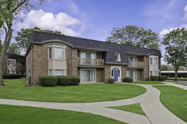 Brick residential building with balconies, green lawn, and pathway under a blue sky.