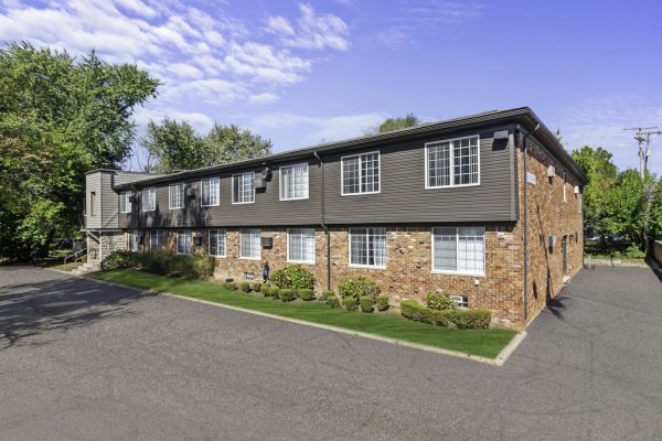 Brick apartment building with large windows surrounded by greenery under a blue sky.