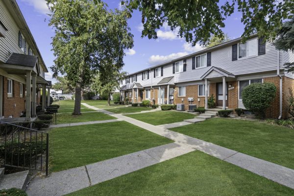 Townhouse complex with brick exteriors, green lawns, and clear blue sky. Ideal residential neighborhood setting.