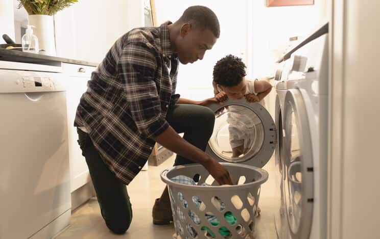 Father and child doing laundry together in home laundry room, teaching and bonding moment.