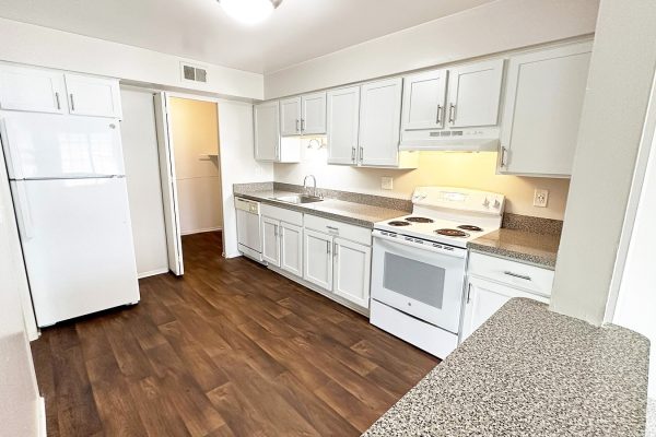 Bright kitchen with white cabinets, granite countertops, and hardwood floors, featuring a stove, fridge, and dishwasher.