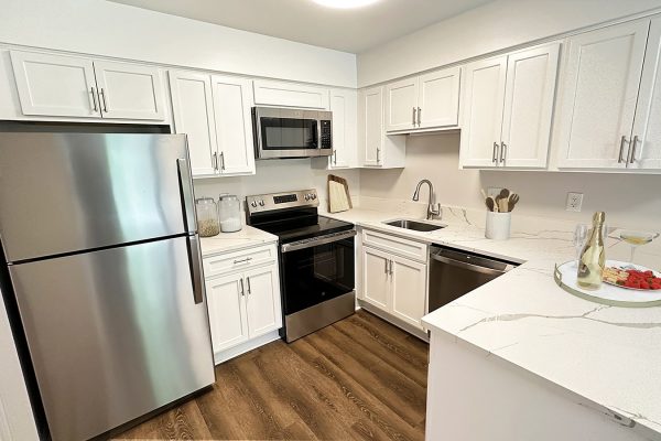 Modern kitchen with white cabinets, stainless steel appliances, and a marble countertop with wine and fruit platter.