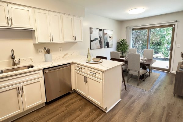 Modern kitchen with white cabinets and marble countertops, leading to a dining area with sliding glass doors.
