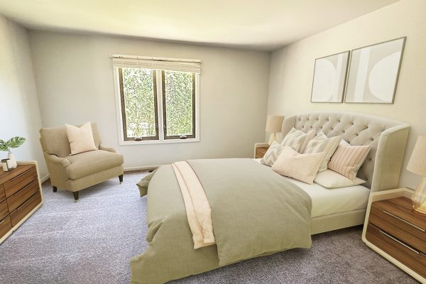 Modern bedroom with beige bedding, upholstered headboard, wooden furniture, and large window with greenery outside.