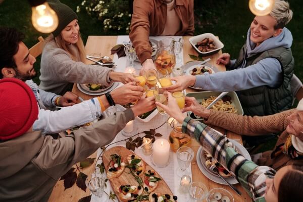 Friends enjoying a cozy dinner outdoors, toasting with drinks over a table of delicious food and candles.