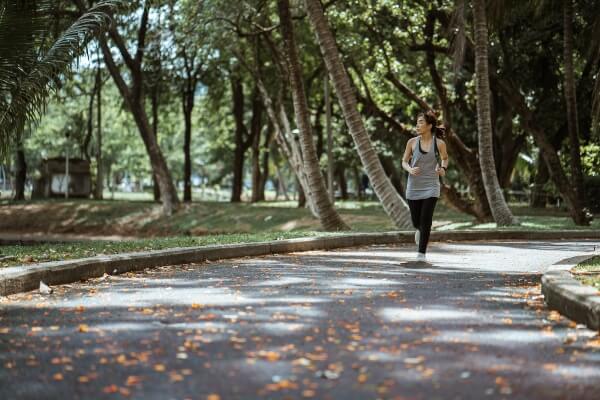 Woman jogging along a park path surrounded by trees on a sunny day.
