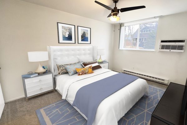 Modern bedroom with a white bed, stylish decor, and natural light from a large window.