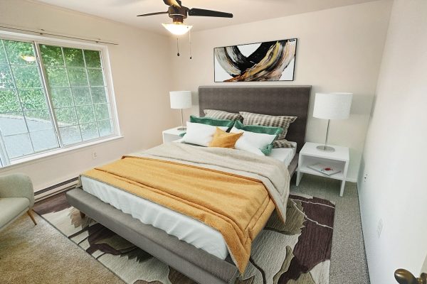 Cozy bedroom with gray bed, colorful pillows, modern decor, and large window letting in natural light.