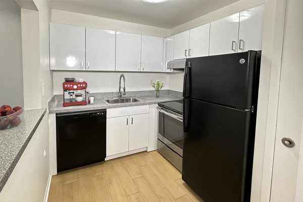 Modern kitchen with black appliances, white cabinets, red espresso machine, and a bowl of fruit on the counter.