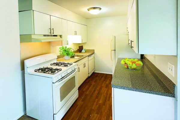 Sleek modern kitchen with white cabinets, gas stove, and wooden floors. Bowl of apples adds a fresh touch.