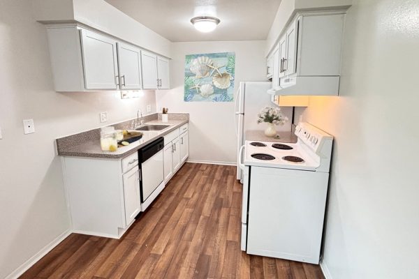 Compact white kitchen with wooden floor, modern cabinets, and decorative art piece. Bright and inviting space.