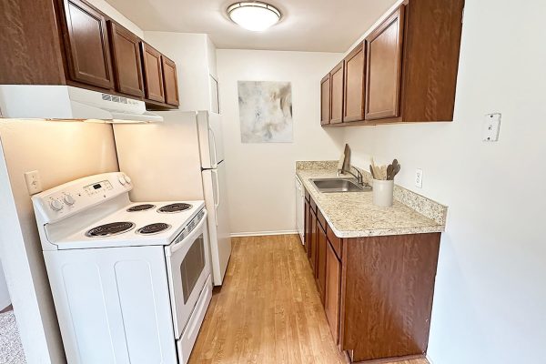 Compact kitchen with wooden cabinets, white appliances, and granite countertops; bright, modern, and efficient space.
