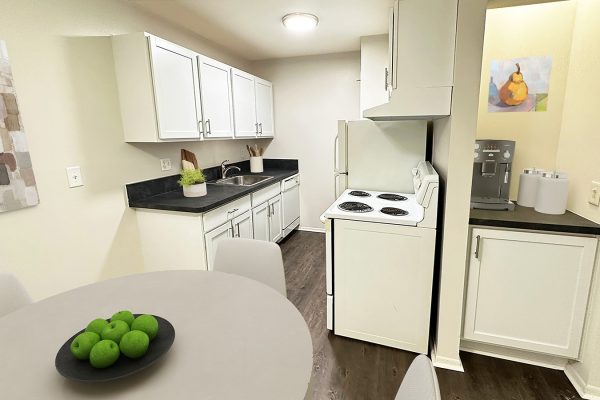 Modern kitchen with white cabinets, black countertops, dining table, fruit bowl, and coffee machine. Cozy and stylish space.