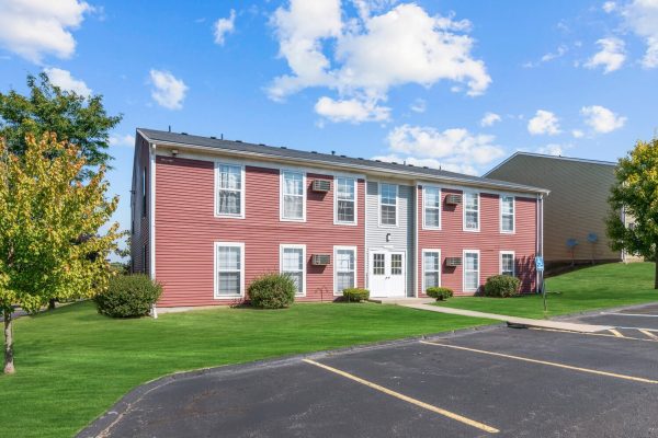 Red apartment building with white trim, lush green lawn, clear blue sky, and accessible parking space.