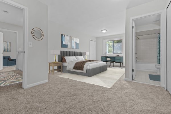 Modern bedroom with gray bed, stylish decor, desk by window, and adjacent bathroom. Cozy and spacious interior.